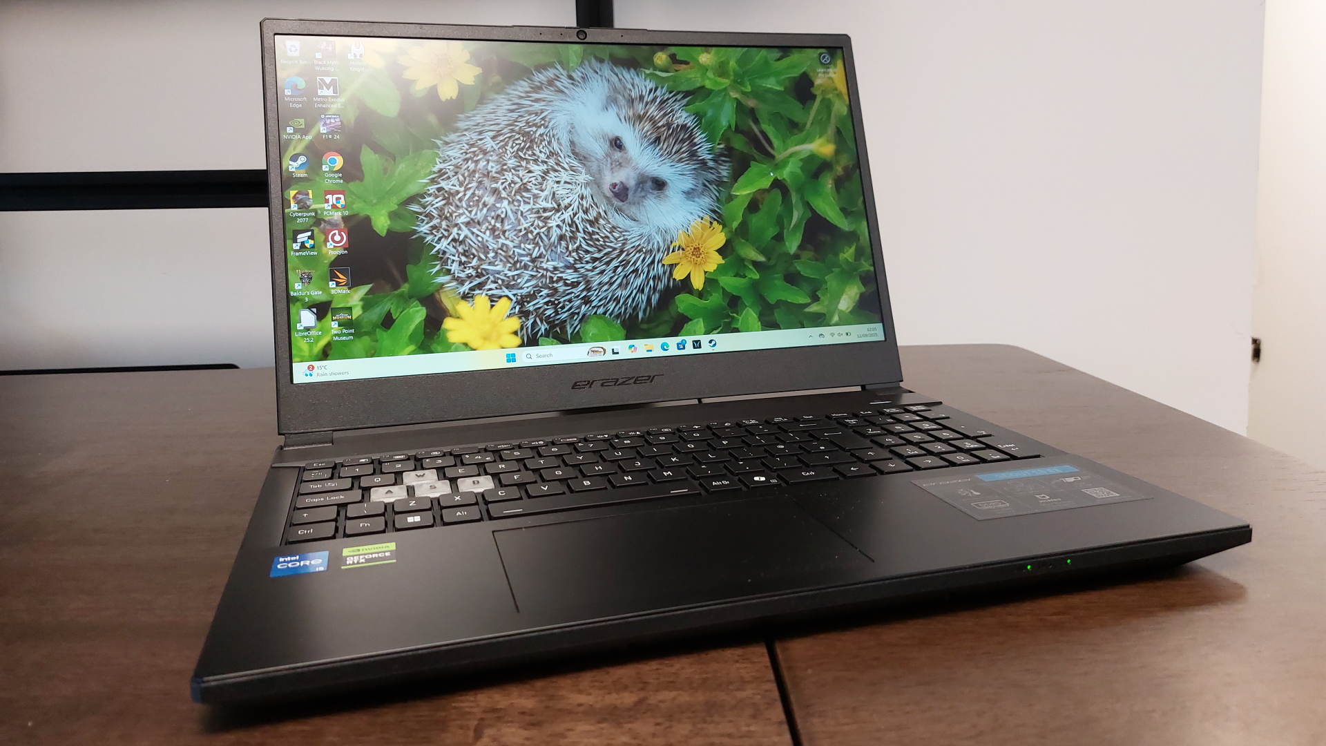 The Erazer Scout 15 E1 RTX 5050 gaming laptop is seen on a wooden desk in a brightly lit, neutral toned office.