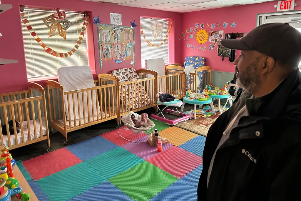 a man looks into pink room full of cribs at a child care center
