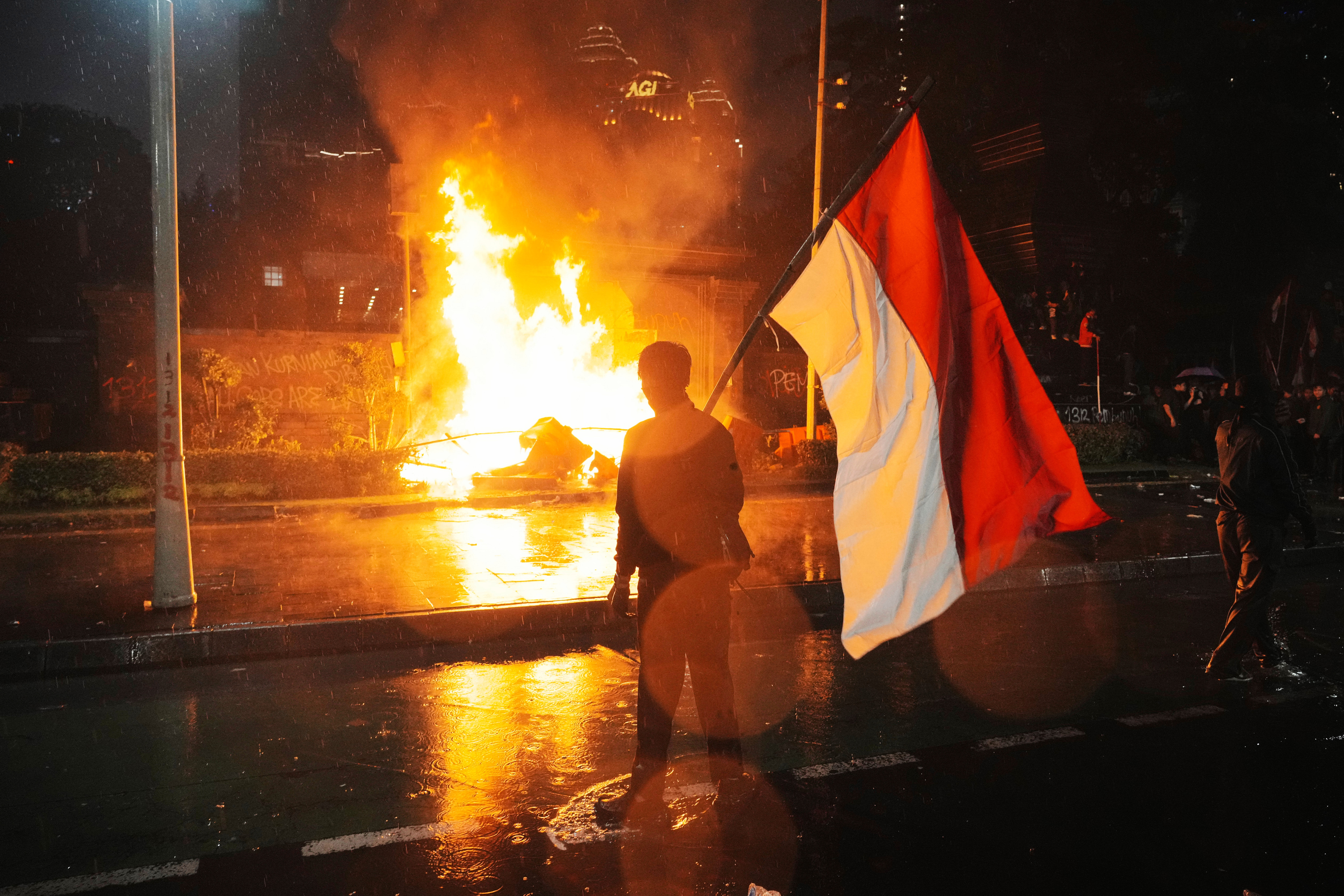 A man carries Indonesian national flag as a traffic police post is burned during a protest following the death of a delivery rider in clashes between riot police and students protesting against lawmakers' allowances, outside the Regional Police Headquarters in Jakarta, Indonesia, Friday, Aug. 29, 2025. (AP Photo/Tatan Syuflana)