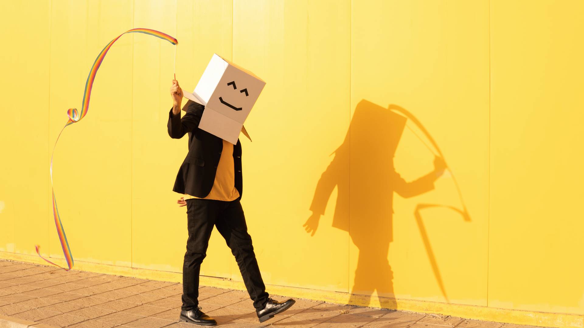 Man in smiley face box spinning rainbow colored rhythmic gymnastics ribbon on sunny day - stock photo