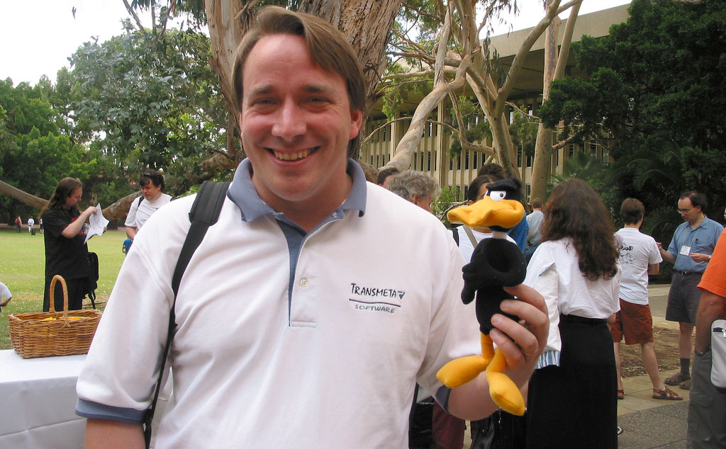 Linus Torvalds smiling while holding a plushie of Daffy Duck.