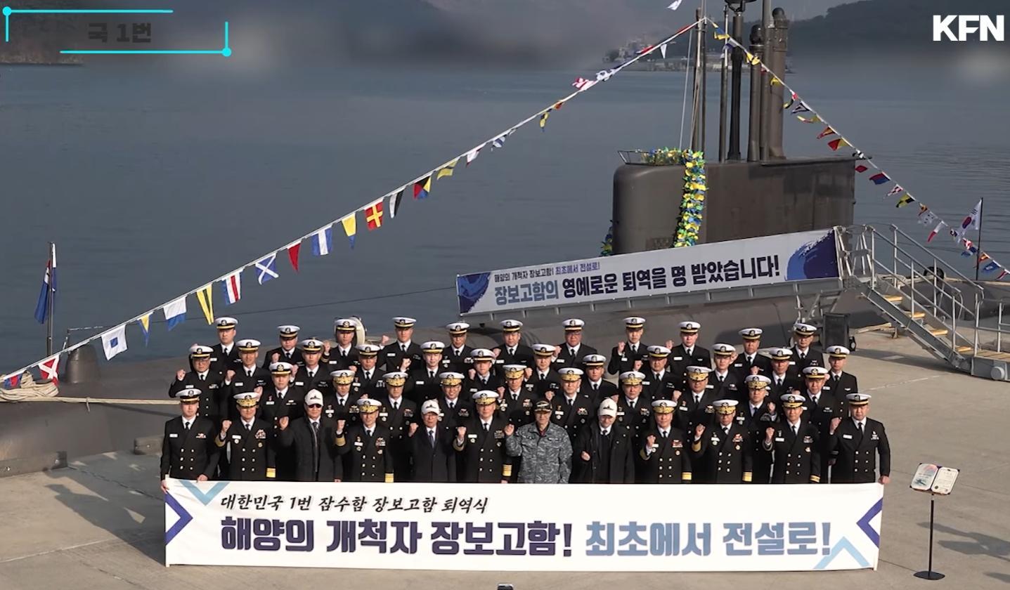横幅上的谚文意为:“大韩民国1号潜水舰张保皋号退役仪式 海洋的开拓者张保皋号!从第一艘驶向传奇!”舷梯上的谚文意为“海洋的开拓者张保皋号!从第一艘驶向传奇!张保皋号已获准光荣退役”
