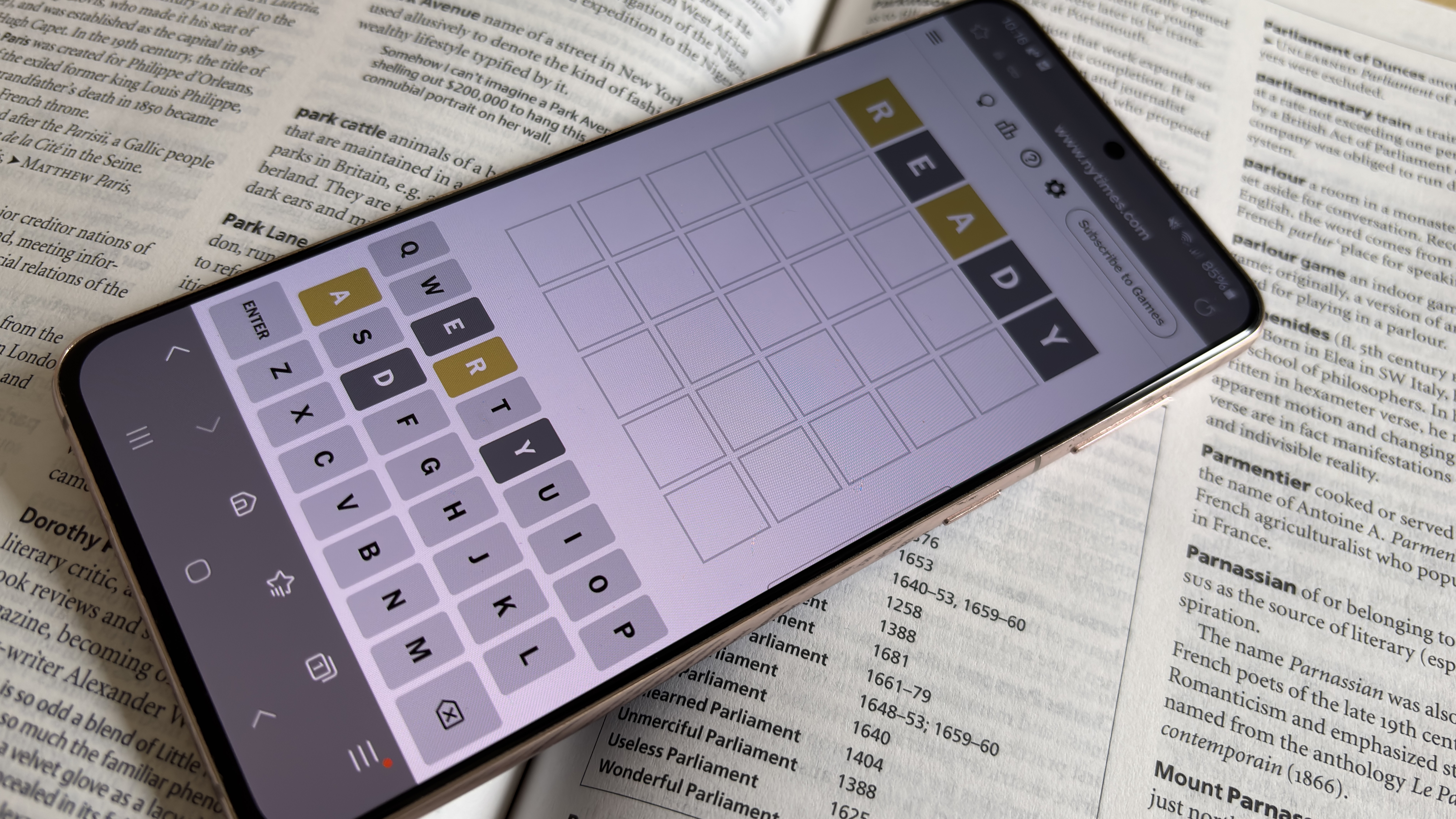 A phone displaying a game of Wordle, on top of a dictionary