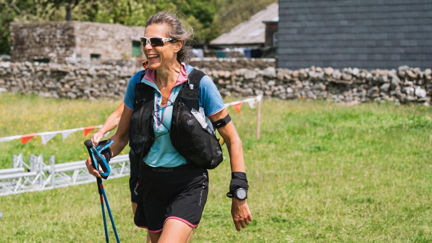 Anna Troup, who is kitted out in trail running attire including shorts, running rucksack, poles, sunglasses and a sports watch, smiles as she reaches a rest point during the Summer Spine Race.