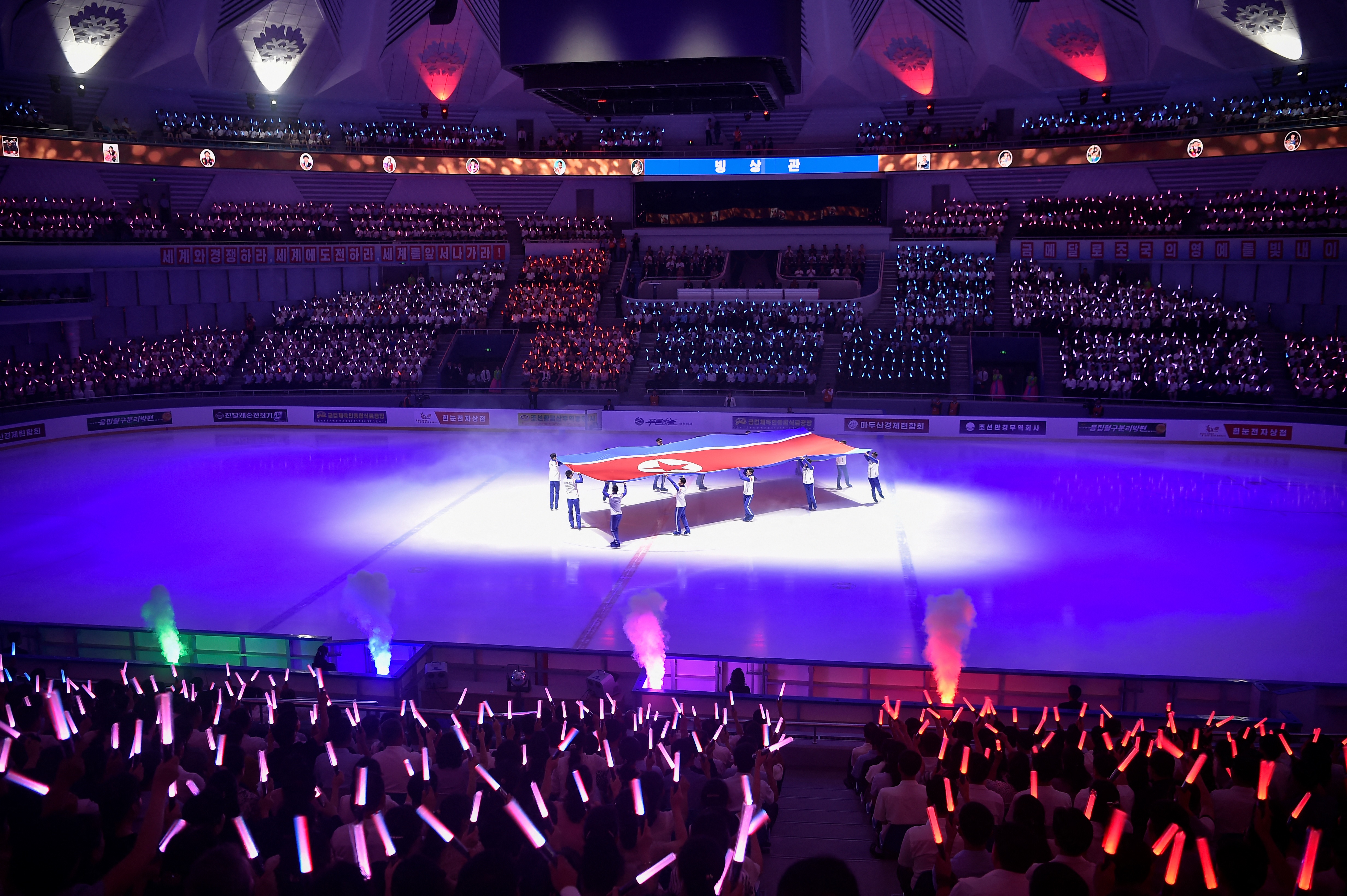 A large North Korean flag is displayed as spectators waves light sticks during the opening ceremony of the recently upgraded Pyongyang Ice Rink in Pyongyang on August 14, 2025. (Photo by KIM Won Jin / AFP)