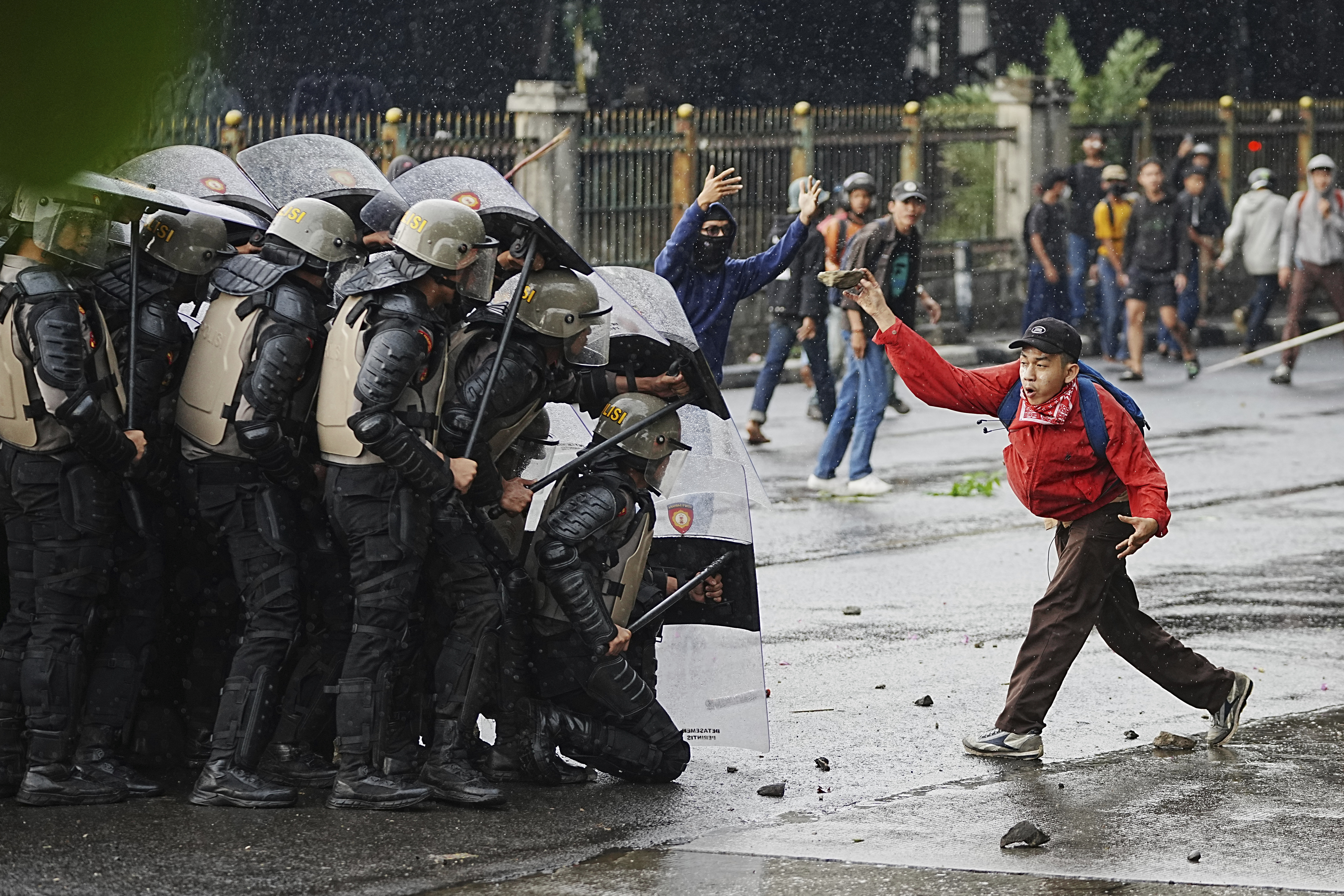 A protester throws rock at riot police officers during a protest against lavish allowances given to parliament members, in Jakarta, Indonesia, Thursday, Aug. 28, 2025. (AP Photo/Achmad Ibrahim)