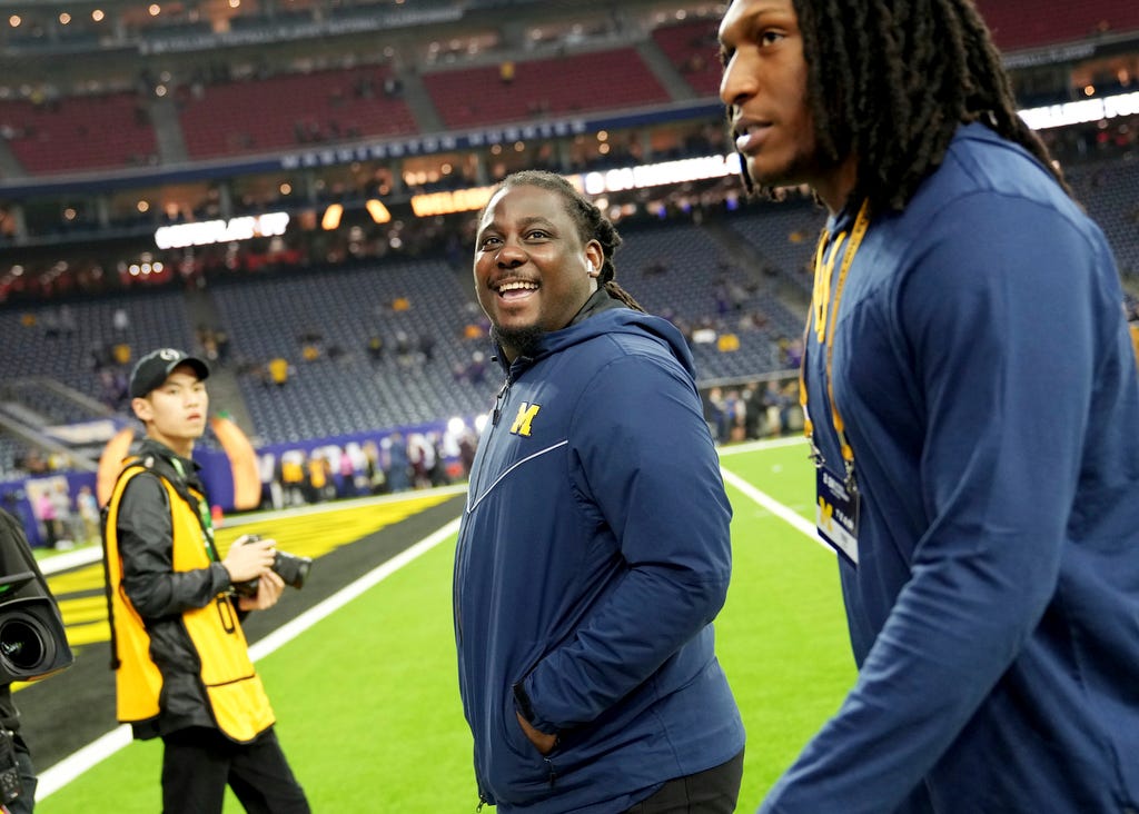 Michigan football staffer Denard Robinson, center, smiles at someone in the stands as he walks into the locker room with the team before the start of the College Football Playoff national championship game against Washington at NRG Stadium in Houston on Jan. 8, 2024.