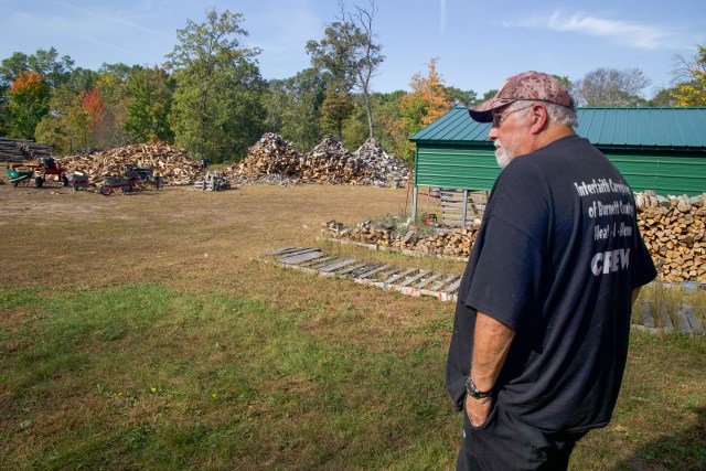 man walking outside toward piles of firewood