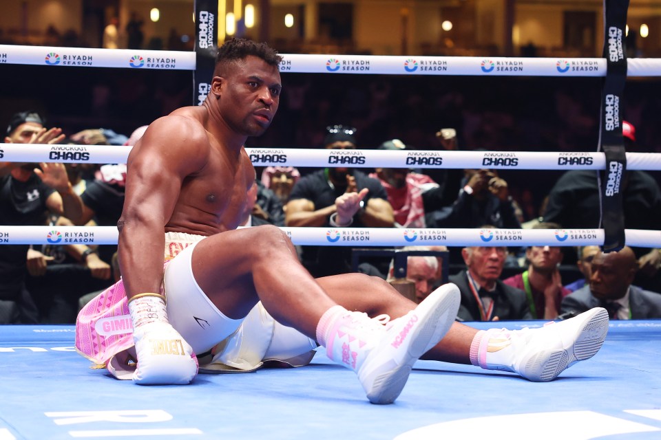 Francis Ngannou sitting in a boxing ring after being knocked down.