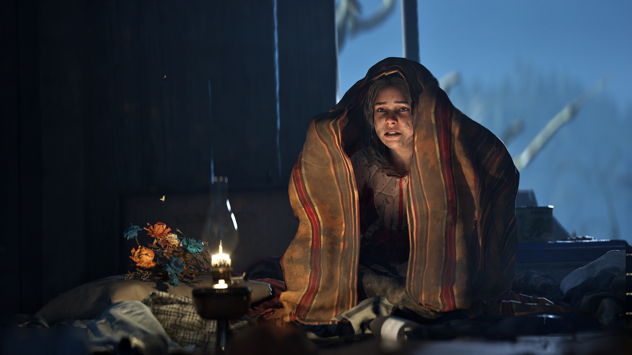 A young girl sitting outside and wrapped in a blanket. She looks frightened in the dark, sitting with only a bundle of flowers and oil lamp.